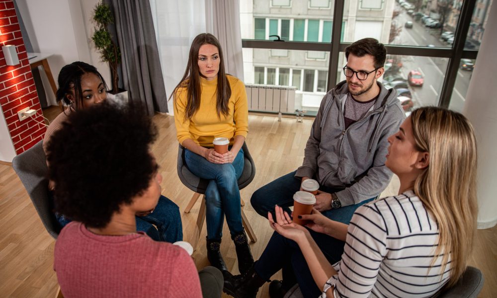 Diverse group of people sitting in circle in group therapy session.