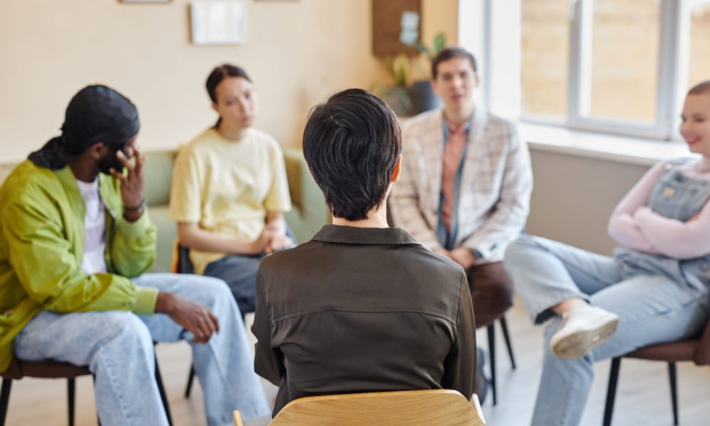 Rear view of specialist sitting on chair and talking to young people during psychotherapy in office